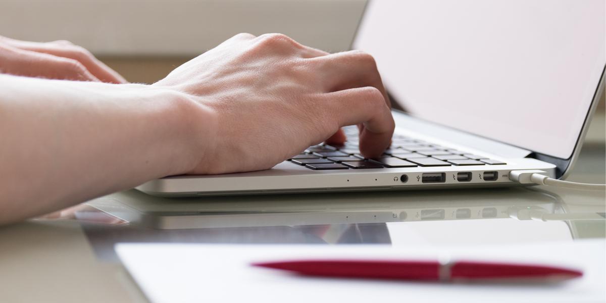 person typing on a computer with pad and pen in foreground